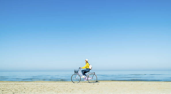 Junge Frau auf dem Fahrrad am Strand an einem sonnigen Tag - DAF00038