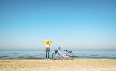 Frau betrachtet die Aussicht, während sie mit dem Fahrrad am Strand steht - DAF00039