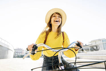 Happy woman in hat standing with bicycle on sunny day - DAF00048