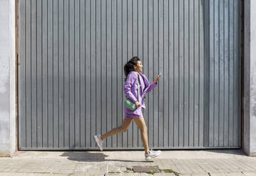 Mid adult woman running by gray wall - AFVF08629