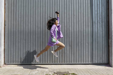 Excited woman jumping by gray wall - AFVF08631