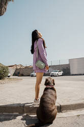 Mid adult woman with pet dog standing on footpath - AFVF08645