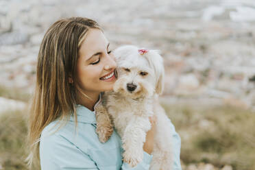 Beautiful woman smiling while embracing dog - MIMFF00716