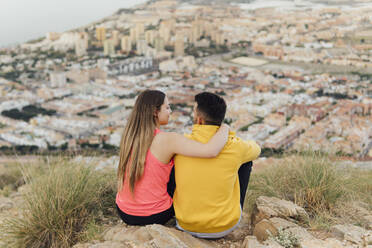 Young girlfriend sitting with arm around of boyfriend on hill - MIMFF00719