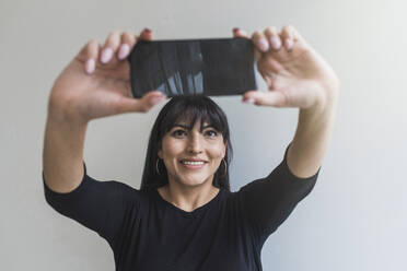 Mittlere erwachsene Frau, die zu Hause ein Selfie mit ihrem Smartphone macht - DSIF00414