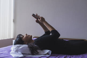 Mid Adult Frau Text-Messaging auf Smartphone im Schlafzimmer - DSIF00420