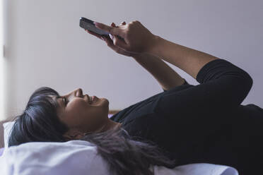 Smiling woman using mobile phone while lying down at home - DSIF00421