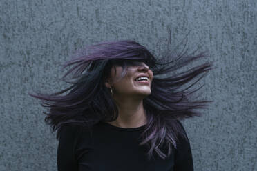 Playful woman tossing hair in front of wall - DSIF00424