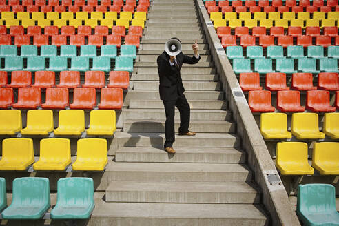 Businessman with bullhorn on sunny steps in stadium - FSIF05615