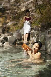 Junge Frauen entspannen und lesen am sonnigen Onsen-Pool - FSIF05620