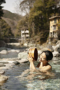 Glückliche junge Frau mit Eimer im sonnigen Pool im Onsen, Izu, Japan - FSIF05622