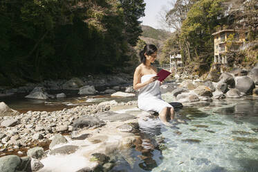 Junge Frau im Handtuch liest Buch am sonnigen Pool im Onsen, Izu, Japan - FSIF05624