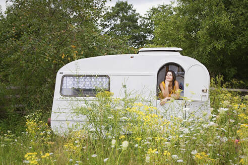 Young woman relaxing inside camper trailer in idyllic meadow - FSIF05695