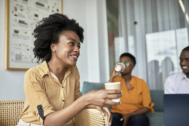 Smiling female professional holding disposable coffee cup at coworking office - ZEDF04051