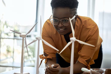 Woman wearing eyeglasses examining wind turbine models at office - ZEDF04101