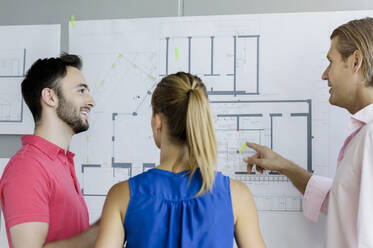 Male design professional explaining technical drawing to colleagues in office - BMOF00551