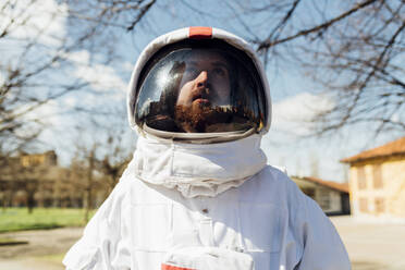 Nachdenklicher männlicher Astronaut im Raumanzug, der an einem sonnigen Tag nach oben schaut - MEUF02370