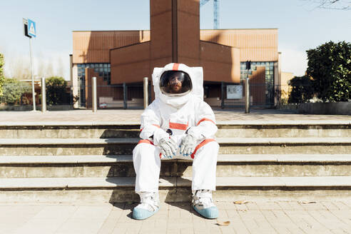 Männlicher Astronaut im Raumanzug auf einer Treppe sitzend an einem sonnigen Tag - MEUF02373