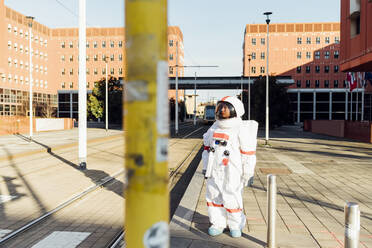 Weibliche Astronautin schaut weg, während sie in der Nähe von Fahrgassen auf einem Fußweg in der Stadt steht - MEUF02374