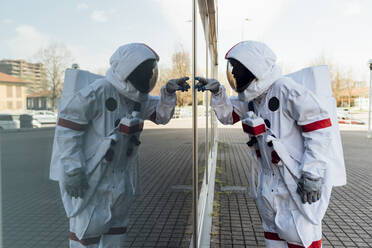 Männlicher Astronaut im Raumanzug berührt die Glaswand in der Stadt - MEUF02388