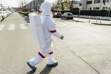 Junge Astronautin im Raumanzug, die an einem sonnigen Tag auf der Straße läuft - MEUF02391