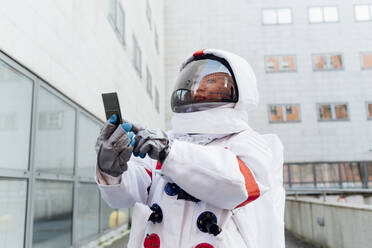 Weibliche Astronautin im Raumanzug benutzt ein Smartphone außerhalb des Gebäudes - MEUF02397