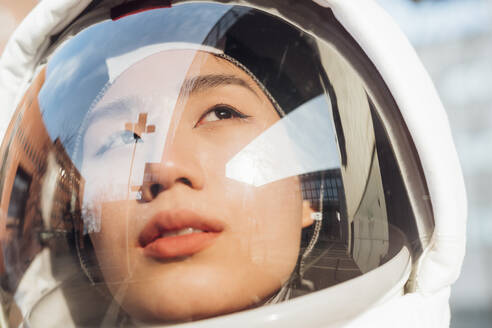 Weibliche Astronautin, die an einem sonnigen Tag durch einen Weltraumhelm wegschaut - MEUF02413