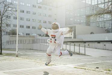 Astronautin in der Luft mit ausgestreckten Armen in der Nähe eines Gebäudes in der Stadt - MEUF02420
