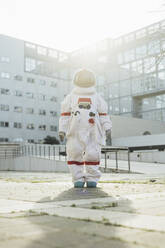 Young female astronaut in space suit standing on footpath near building - MEUF02422