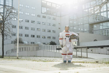 Weibliche Astronautin mit Weltraumhelm vor einem Gebäude in der Stadt an einem sonnigen Tag - MEUF02424