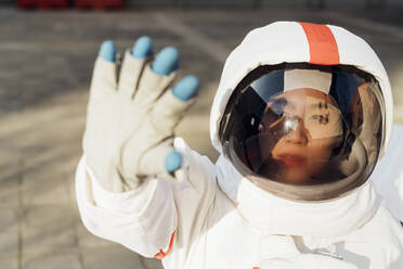 Junge Astronautin im Raumanzug, die ihre Augen vor dem Sonnenlicht schützt - MEUF02434