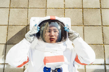 Weibliche Astronautin mit Helm auf dem Gehweg liegend an einem sonnigen Tag - MEUF02440
