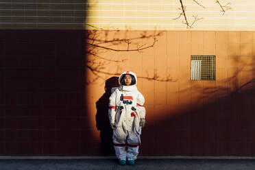 Woman astronaut in space suit standing by wall during sunset - MEUF02456