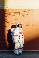 Young female astronaut standing by wall with tree shadow during sunset - MEUF02457