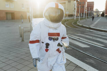 Astronautin im Raumanzug auf dem Fußweg in der Nähe von Straßenbahnschienen in der Stadt - MEUF02459