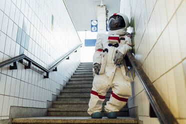Woman astronaut leaning on railing in subway - MEUF02464