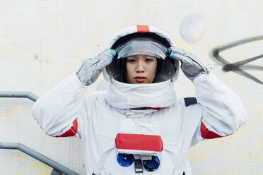 Female astronaut holding helmet while standing by wall - MEUF02470
