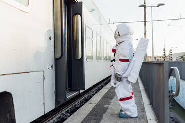 Junge Astronautin steht am Eingang eines Zuges am Bahnhof - MEUF02472