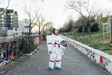 Female astronaut wearing space suit holding helmet while standing on footpath - MEUF02480