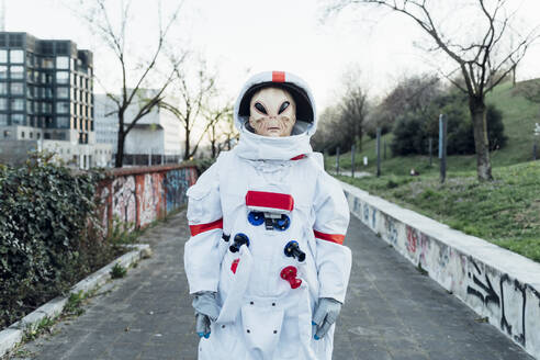 Junge Astronautin mit Alien-Maske auf einem Fußweg in der Stadt - MEUF02482