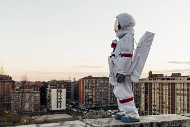 Astronautin steht auf einer Stützmauer und blickt auf die Stadt - MEUF02487