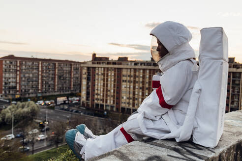 Junge Astronautin sitzt bei Sonnenuntergang auf einer Stützmauer - MEUF02488