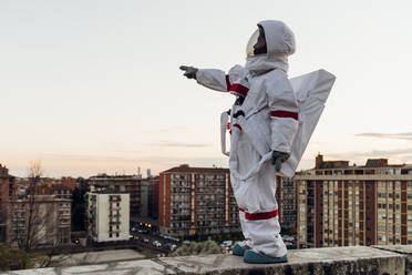 Female astronaut in space suit pointing while standing on retaining wall during sunset - MEUF02489