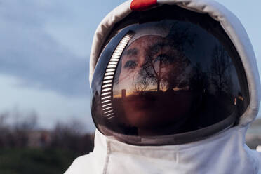 Nachdenklich dreinblickende Astronautin mit Weltraumhelm bei Sonnenuntergang - MEUF02499