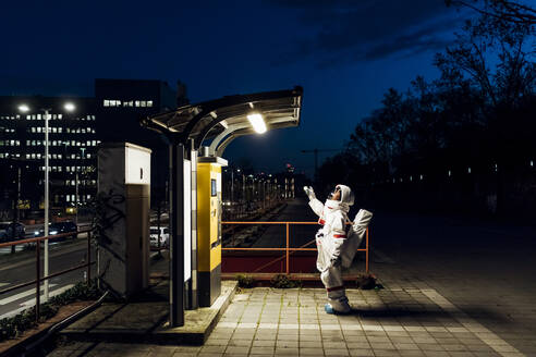 Junge Astronautin steht in der Nähe einer beleuchteten Telefonzelle in einer nächtlichen Stadt - MEUF02508