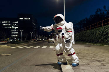 Weibliche Astronautin im Raumanzug, die nachts auf dem Gehweg in der Nähe der Straße steht - MEUF02512