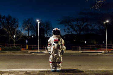 Young female astronaut in space suit standing on footpath at night - MEUF02513