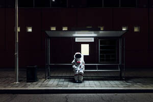 Female astronaut sitting at bus stop during night - MEUF02515