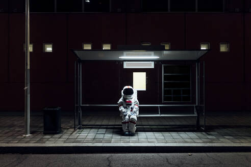 Astronautin sitzt nachts an der Bushaltestelle - MEUF02515