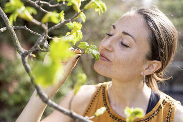 Mittlere erwachsene Frau mit geschlossenen Augen riecht an einem Zweig im Garten - WPEF04294